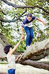 Mature woman holding sons hand whilst climbing park tree branch