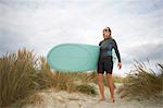 Portrait of senior woman on sand, holding surfboard