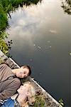 Overhead view of young couple lying on river footbridge