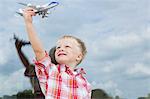 Boy holding up toy airplane in front of house window