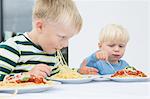 Boy and toddler brother eating spaghetti on patio