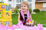 Portrait of female toddler with birthday cake and pink ribbons in garden