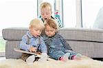 Boy and two toddlers reading childrens book on living room floor