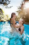 Two teenage girls jumping and splashing in swimming pool