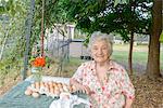 Senior woman posing beside tray of eggs on farm