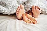 Bare feet of father and son lying in bed