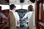 Rear view of male and female pilots in cockpit of private jet