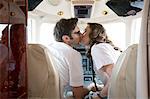 Rear view of male and female pilots kissing in cockpit of private jet