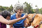 Two mature female friends, petting dog, outdoors