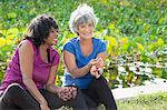 Mature female friends sitting in park, eating grapes