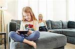 Mother and daughter using digital tablet on sofa in living room