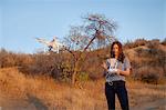 Female commercial operator on scrubland flying drone, looking down, Santa Clarita, California, USA