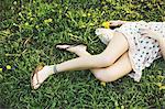 Waist down high angle view of young woman lying on grass wearing dress, flipflops and ankle bracelet