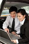 Businesspeople working on laptop in back of car