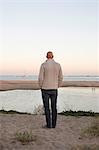 Bald man standing on a sandy beach by the ocean.