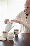 Man sitting at a table, pouring a cup of coffee.