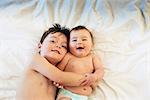 Two children, a brother and baby sister lying down playing together.