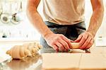 A baker working on a floured surface, rolling up dough squares into croissant shapes before baking.