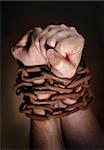 Hands of a man with a rusty chain around the wrists. Short depth of field, the sharpness is in the fist.