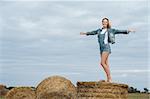 beautiful woman with arms raised standing on haystack