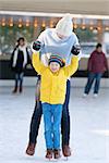 little boy and his mother enjoying cold winter weather and ice skating at outdoor rink