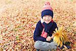 happy smiling little boy holding autumn leaves bouquet and enjoying fall weather in the park