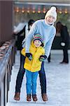 young mother teaching her little son ice skating at outdoor skating rink