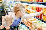 positive 6-year old boy buying healthy fruits at supermarket or grocery store helping his parents