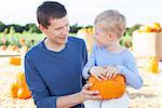 cheerful little boy and his young father holding pumpkin enjoying halloween time at pumpkin patch