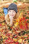 smiling little boy with bouquet lying in the colorful autumn leaves enjoying nice weather in the park