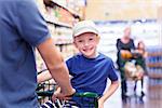 family of two shopping together at supermarket with kid sitting in the cart