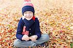 smiling little boy sitting in the colorful autumn leaves enjoying nice weather in the park