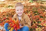 smiling little boy with bouquet sitting in the colorful autumn leaves enjoying nice weather in the park