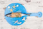 Delicious fresh mackerel fish on wooden kitchen board with seashells and sea star on white textured wooden background. Culinary healthy cooking.