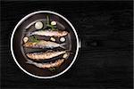 Delicious fresh anchovy fish with fresh rosemary herbs on pan on black wooden background. Culinary healthy seafood cooking.