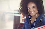 Smiling woman with afro listening to music with headphones on bus