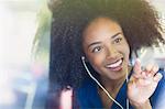 Smiling woman with afro and headphones drawing heart-shape on bus window