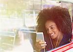 Smiling woman with afro listening to music with headphones and mp3 player on bus