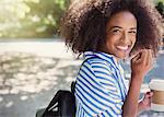 Portrait enthusiastic woman with afro drinking coffee in park