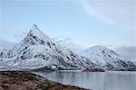 Snow covered mountains along cold lake, Lofoten Islands, Norway