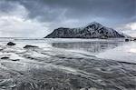 Snow covered rock formation on cold ocean beach, Skagsanden Beach, Lofoten Islands, Norway