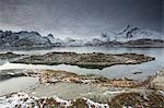 Snow covered mountain range behind craggy bay, Sund, Lofoten Islands, Norway