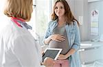 Doctor with digital tablet talking with pregnant teenage patient in examination room