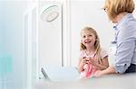 Pediatrician watching girl patient playing with stethoscope in examination room