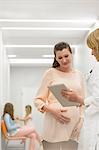 Doctor with digital tablet talking to pregnant patient in clinic corridor