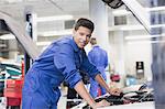 Portrait confident mechanic leaning over car engine in auto repair shop