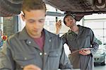 Mechanic with clipboard working under car in auto repair shop