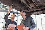 Mechanics with clipboards working under car in auto repair shop