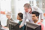 Professor helping student at computer in adult education classroom