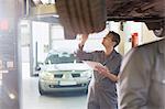 Mechanic with clipboard under car in auto repair shop